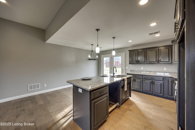 kitchen featuring visible vents, baseboards, a center island with sink, light wood-style flooring, and a sink