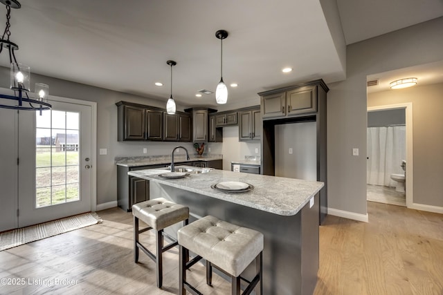 kitchen featuring a center island with sink, light wood-type flooring, baseboards, and a sink