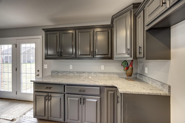 kitchen featuring a healthy amount of sunlight, gray cabinetry, baseboards, and light stone countertops