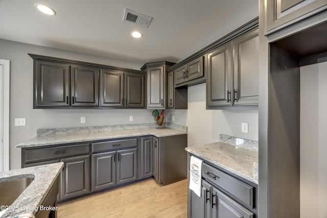 kitchen with light wood-style flooring, light stone counters, recessed lighting, and visible vents