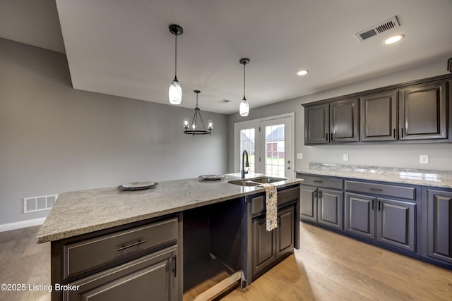 kitchen featuring a sink, visible vents, light wood-type flooring, and light stone countertops