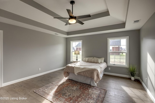 bedroom featuring visible vents, multiple windows, a raised ceiling, and wood finished floors