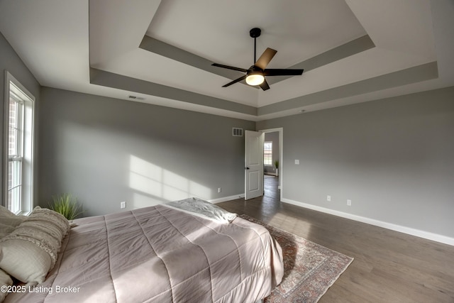 bedroom featuring dark wood-style floors, visible vents, baseboards, and a tray ceiling