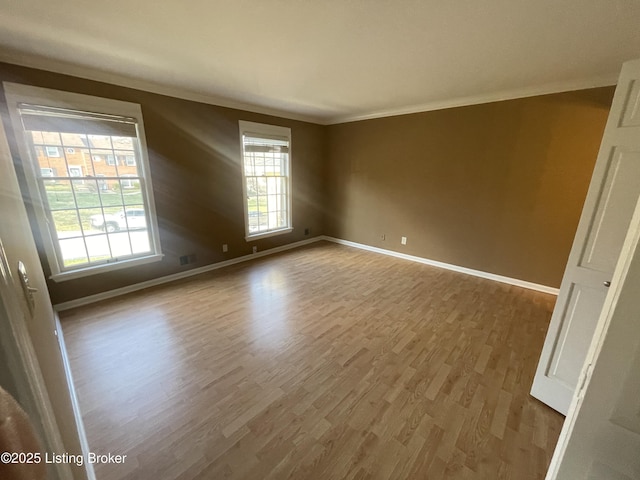 empty room featuring crown molding, wood finished floors, baseboards, and visible vents