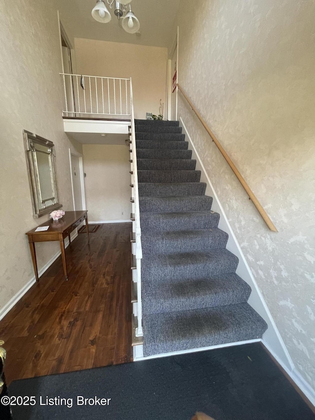 stairs with a textured wall, a notable chandelier, baseboards, and wood finished floors