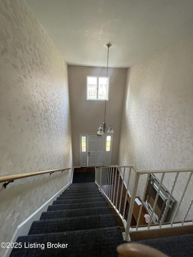 staircase with a high ceiling, an inviting chandelier, and a textured wall