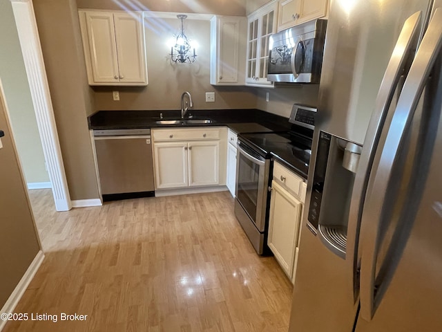 kitchen with light wood-type flooring, a sink, dark countertops, stainless steel appliances, and white cabinets