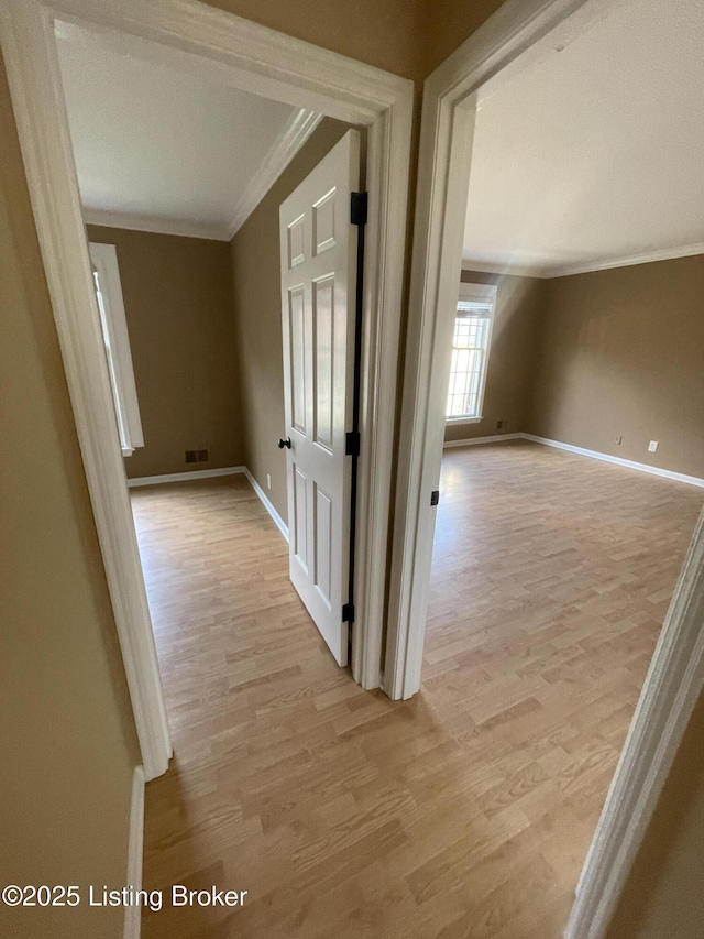 hallway with light wood finished floors, visible vents, baseboards, and ornamental molding