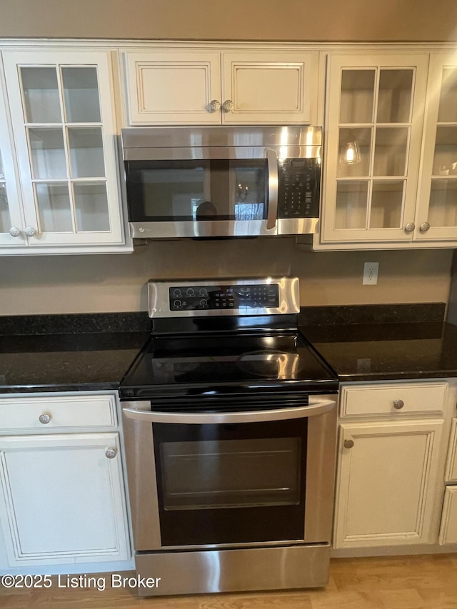 kitchen with dark stone countertops, white cabinets, glass insert cabinets, and appliances with stainless steel finishes