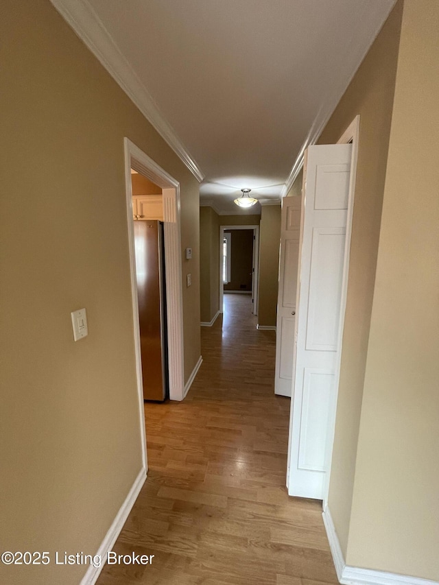 corridor featuring light wood finished floors, crown molding, and baseboards