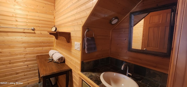 bathroom featuring vaulted ceiling, wooden walls, and a sink