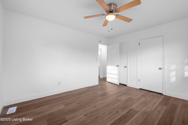 unfurnished bedroom featuring wood finished floors, visible vents, baseboards, ceiling fan, and multiple closets