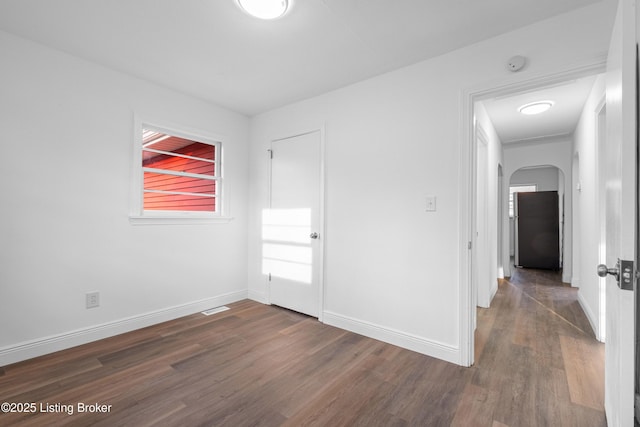 empty room featuring arched walkways, visible vents, baseboards, and dark wood-style flooring