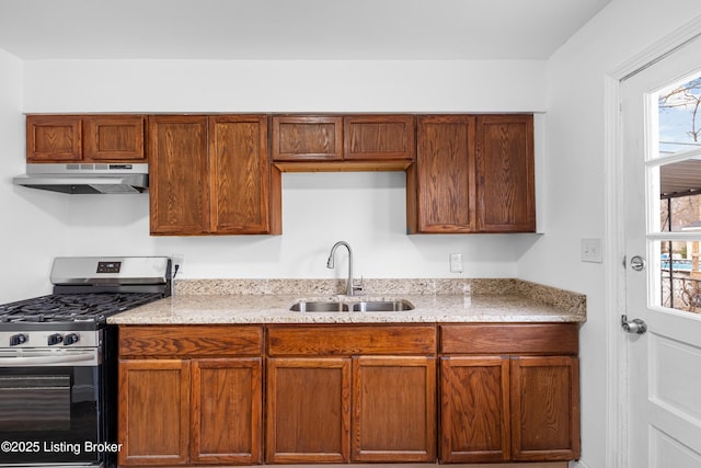 kitchen featuring under cabinet range hood, light stone countertops, a sink, and gas stove