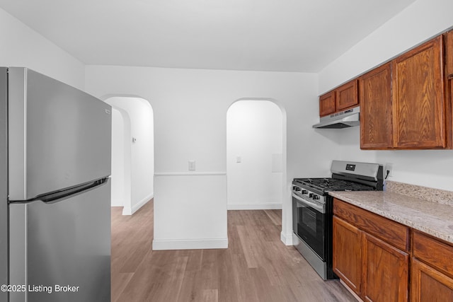 kitchen with under cabinet range hood, light wood finished floors, arched walkways, and stainless steel appliances