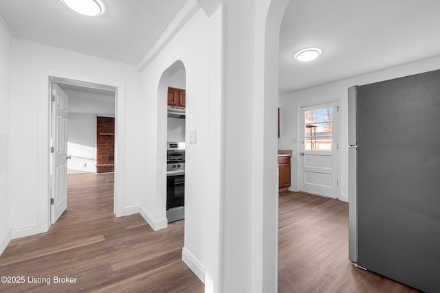 hallway with baseboards, arched walkways, and wood finished floors