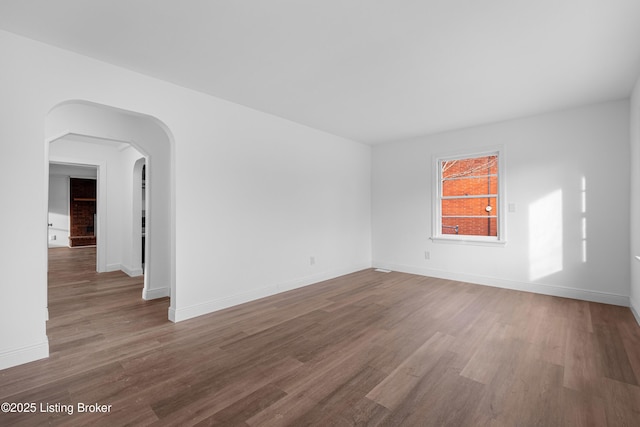 unfurnished room with wood finished floors, arched walkways, and baseboards