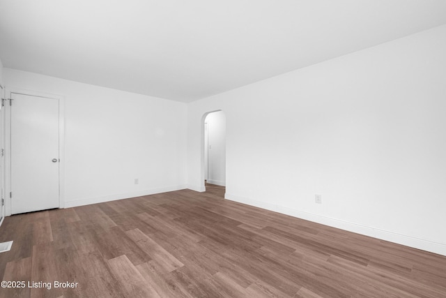 empty room with visible vents, wood finished floors, arched walkways, and baseboards