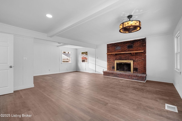 unfurnished living room with visible vents, a brick fireplace, beamed ceiling, and wood finished floors