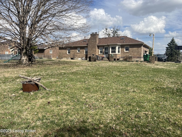 rear view of house featuring a lawn, a chimney, brick siding, and roof with shingles