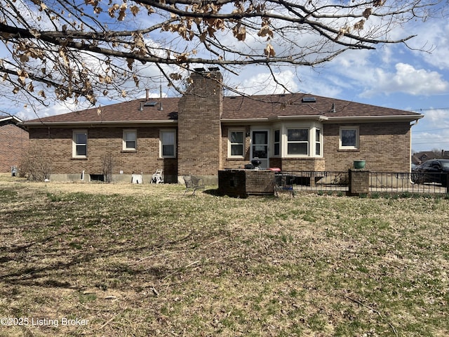 rear view of house featuring brick siding, fence, roof with shingles, a lawn, and a chimney