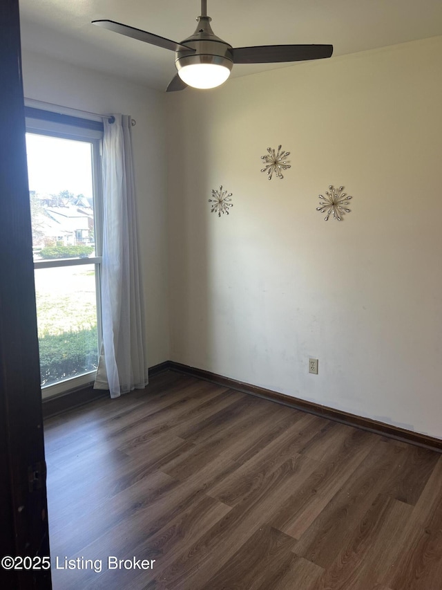 spare room featuring dark wood-style floors, a ceiling fan, and baseboards