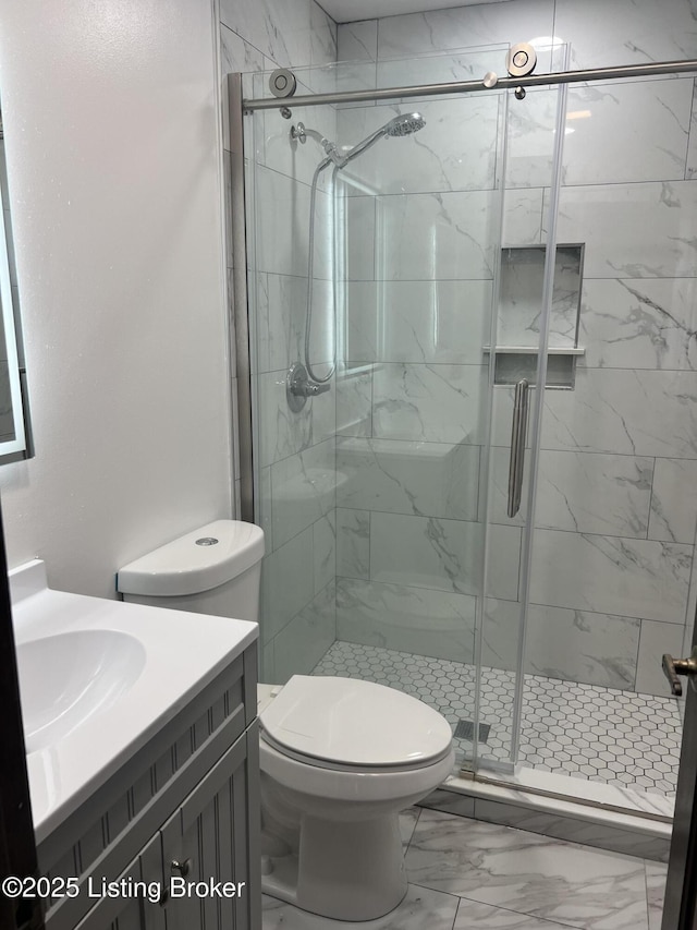 bathroom with a shower stall, vanity, toilet, and marble finish floor