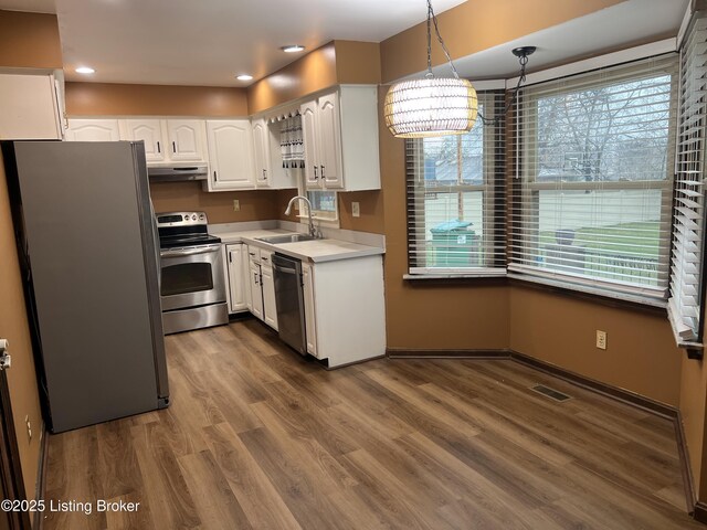 kitchen with dark wood finished floors, a sink, white cabinets, under cabinet range hood, and appliances with stainless steel finishes