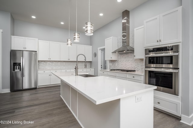 kitchen with a center island with sink, light countertops, appliances with stainless steel finishes, wall chimney exhaust hood, and a sink