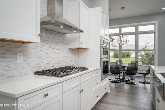 kitchen with dark wood-style floors, white cabinets, appliances with stainless steel finishes, wall chimney exhaust hood, and a notable chandelier