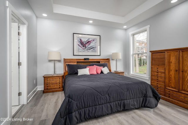 bedroom with a raised ceiling, recessed lighting, wood finished floors, and baseboards