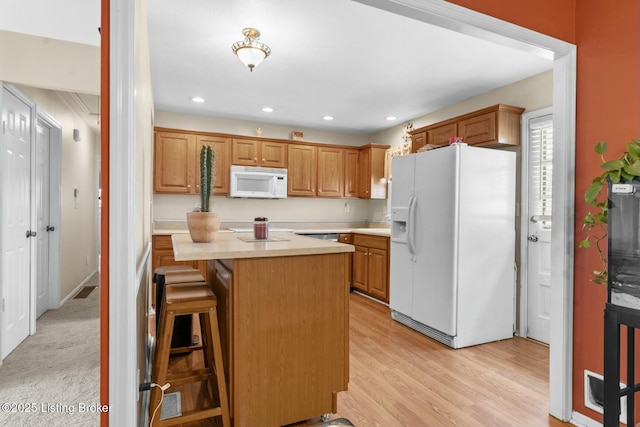 kitchen featuring a kitchen breakfast bar, recessed lighting, white appliances, light wood-style floors, and light countertops