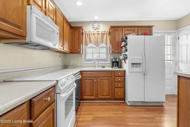 kitchen featuring light wood-style flooring, a sink, white appliances, brown cabinetry, and light countertops