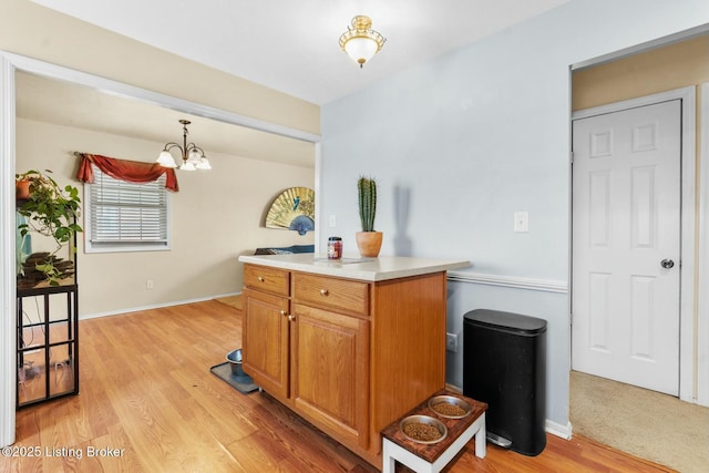 kitchen featuring light wood-type flooring, a notable chandelier, brown cabinetry, light countertops, and hanging light fixtures