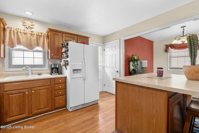 kitchen featuring a sink, brown cabinets, light countertops, and white fridge with ice dispenser