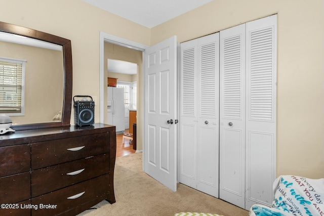 bedroom featuring a closet, light carpet, and white refrigerator with ice dispenser