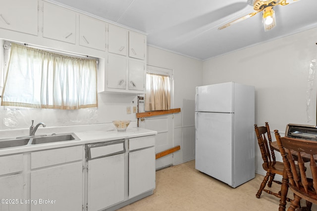 kitchen featuring light floors, freestanding refrigerator, ceiling fan, a sink, and white cabinets