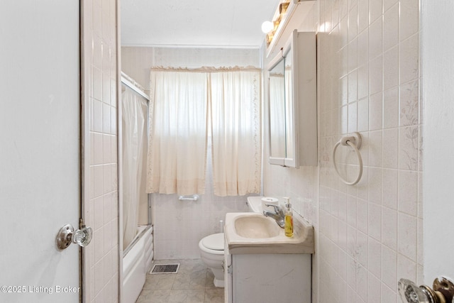 bathroom featuring visible vents, toilet, tile walls, enclosed tub / shower combo, and vanity