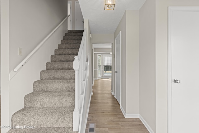 stairway featuring visible vents, a textured ceiling, baseboards, and wood finished floors