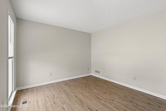 unfurnished room featuring visible vents, baseboards, a textured ceiling, and wood finished floors