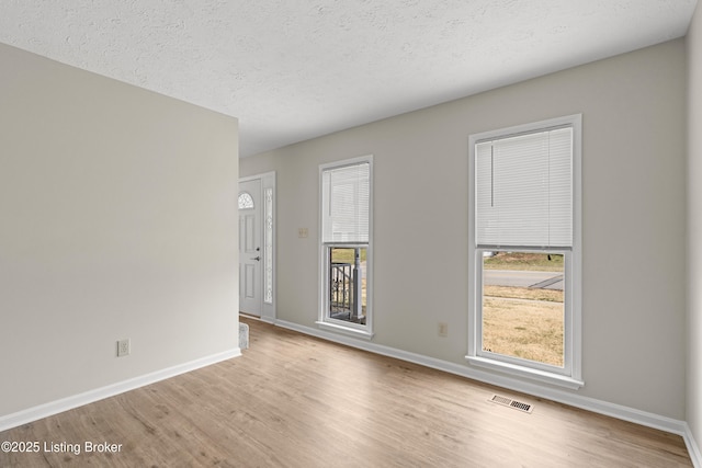 empty room with visible vents, plenty of natural light, baseboards, and wood finished floors