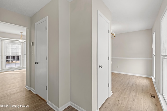 corridor with baseboards, visible vents, and light wood finished floors