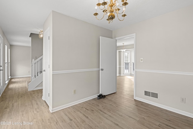 empty room with stairway, wood finished floors, visible vents, baseboards, and an inviting chandelier