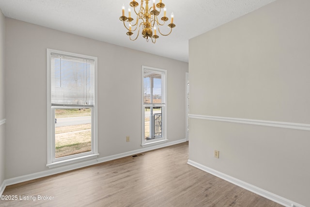 empty room with visible vents, plenty of natural light, a notable chandelier, and wood finished floors