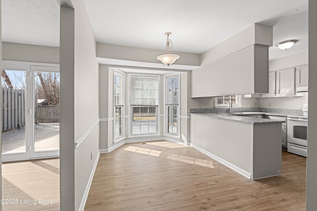 kitchen featuring light wood finished floors, baseboards, pendant lighting, a peninsula, and white electric range