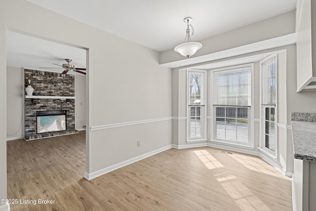 unfurnished dining area featuring light wood finished floors, visible vents, baseboards, a fireplace, and a ceiling fan