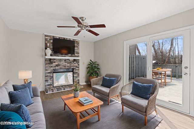 living area featuring light wood finished floors, a fireplace, and a ceiling fan