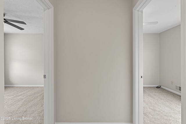 corridor featuring visible vents, baseboards, a textured ceiling, and carpet flooring