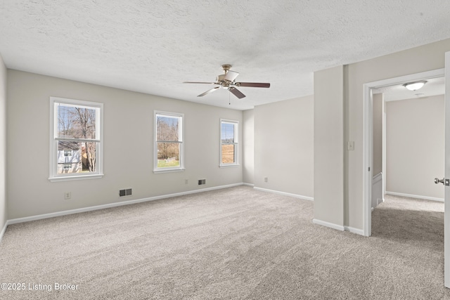 carpeted spare room with visible vents, baseboards, a textured ceiling, and a ceiling fan