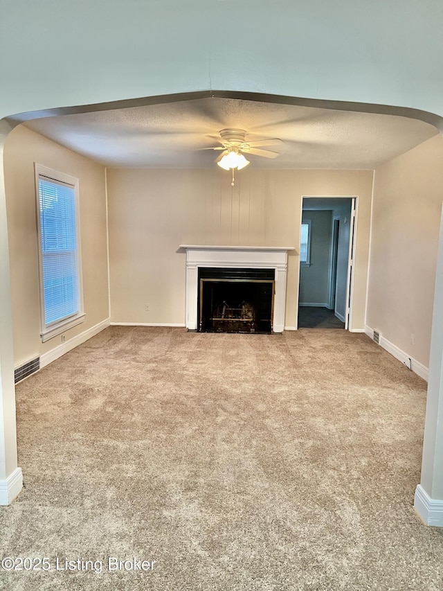 unfurnished living room with visible vents, arched walkways, carpet flooring, and a ceiling fan